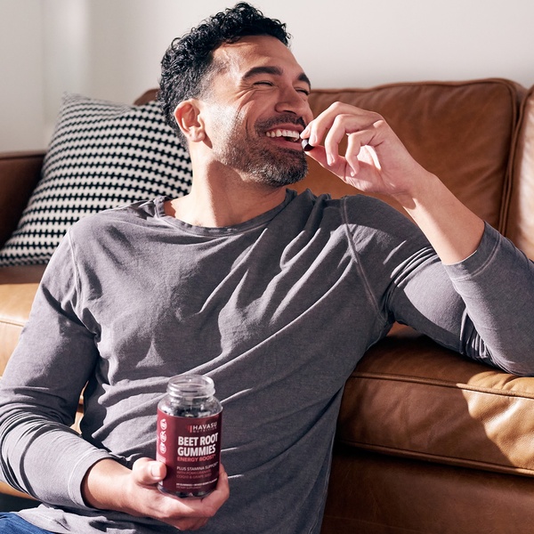 A man smiling on a couch, holding a bottle of beet root gummies, capturing a relaxed and authentic lifestyle moment.